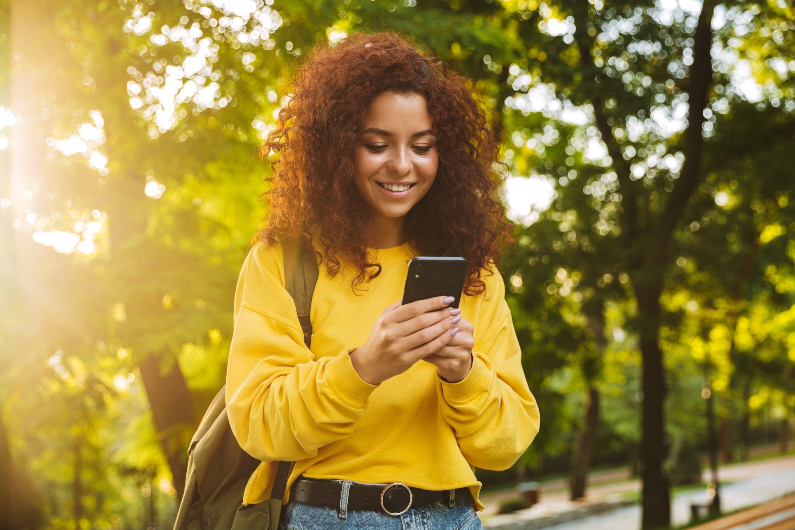 Youth road map header image - Youth woman wearing yellow sweater reading cell phone in park