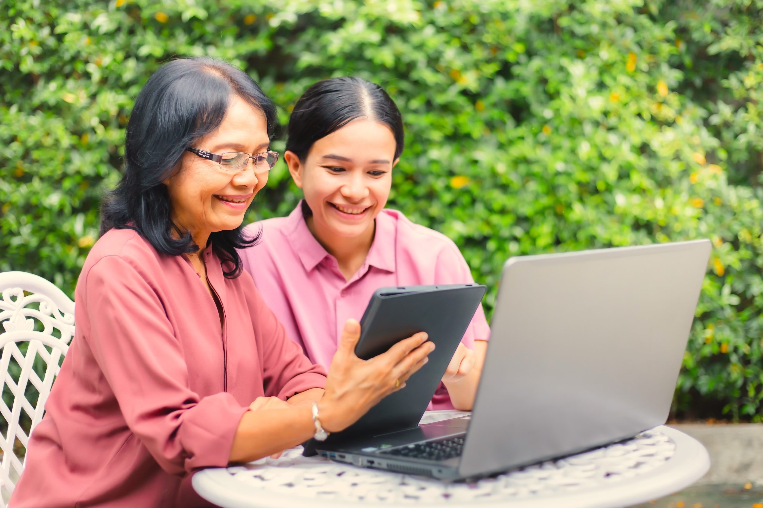 Parent and Caregiver Reference Guide header image - Happy Asian woman teaching her mother to use tablet and laptop in home garden. Senior mature and young woman surfing internet with digital devices together. Middle aged and technology