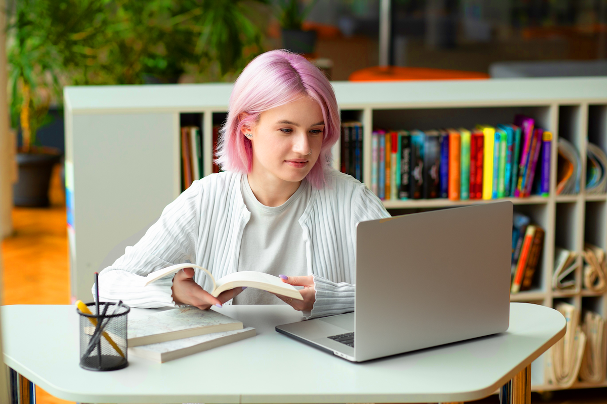 Resources header image - Young woman with pink hair researching on a laptop in a library